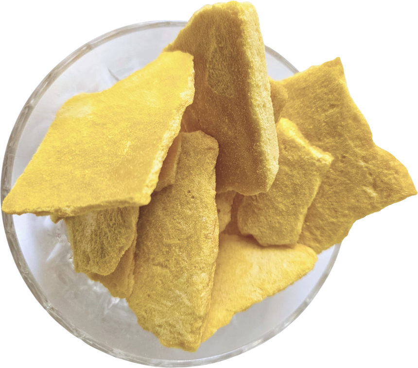A glass bowl of freeze-dried Kesar mango slices: pale gold, brittle, and full of the open honeycomb texture left behind when the water is taken out
